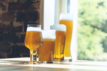 Glasses of different kinds of light beer in sunlight on brick wall background. Cold delicious alcohol drinks are prepared for a big friend's party. Concept of holiday, fun, meeting, oktoberfest.
