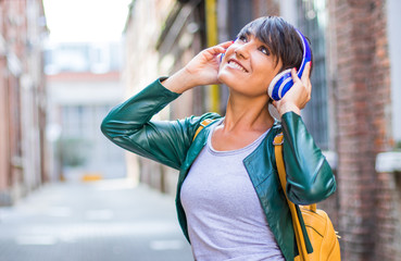Portrait of a happy girl listening music with wireless headphones in the street 
