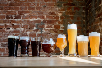 Glasses of dark and light beer and ale in sunlight on brick wall background. Cold delicious alcohol...