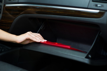 A young woman's hand puts a red folder in the glove compartment in the car
