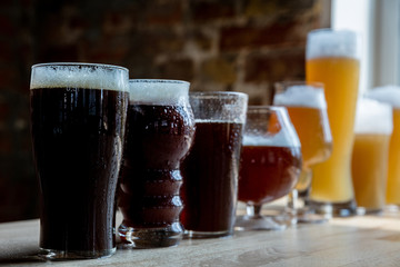 Glasses of dark and light beer and ale in sunlight on brick wall background. Cold delicious alcohol drinks are prepared for a big friend's party. Concept of holiday, fun, meeting, oktoberfest.