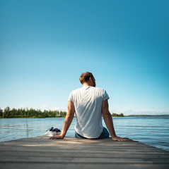 Mann sitzt im Sommer in Finnland auf einem Holzsteg am See - 286725838