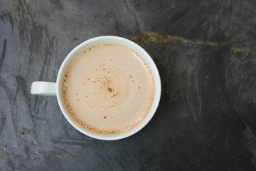 white cup with cappuccino and sweets on a stone black streaked table, top view, close-up, copy space