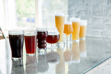 Glasses of dark and light beer and ale in sunlight on brick wall background. Cold delicious alcohol drinks are prepared for a big friend's party. Concept of holiday, fun, meeting, oktoberfest.