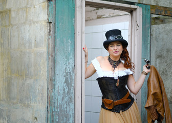 Beautiful redhair steampunk girl with goggles on black hat outside toilet background. Old-fashioned.