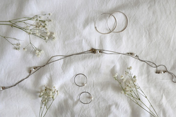 Silver and gold jewelry and gypsophila flowers on white sheets. Top view.