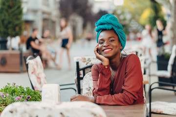 Outdoor portrait of fashionable muslim girl sitting at a table of street cafe