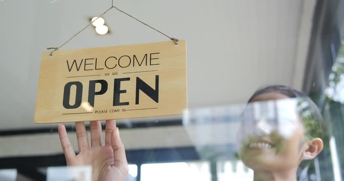 Woman turning open sign in the morning.