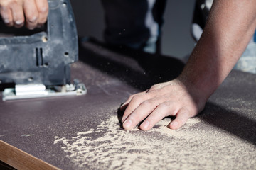 Closeup hand of woodworker with professional cutting tool fretsaw or jigsaw, cut wooden tabletop, sawing plank, brown filings, sawdust. Concept cut a hole for the sink in bathroom