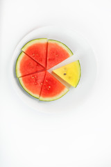 Yellow and red watermelon in a white round plate, on a white background, sliced. The concept of contrast highlight and difference