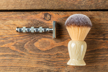 Metallic safety razor and shaving brush on rustic wooden boards background, barber shop concept