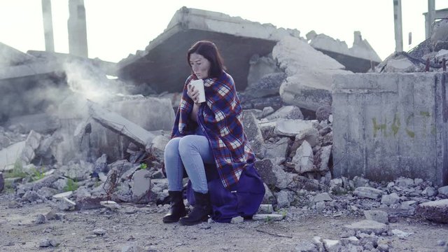 woman victim of natural disaster or terrorist attack sitting after rescue amidst Smoking ruins