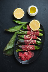 Carpaccio beef with salad leaves and parmesan, flatlay over black stone background, studio shot