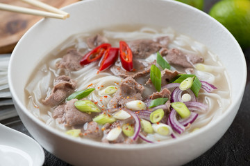Closeup of a white bowl with traditional vietnamese pho bo soup, selective focus
