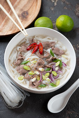 Bowl of pho bo soup with beef meat over brown stone background, vertical shot