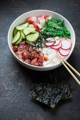 Poke with tuna served in a white bowl, vertical shot on a dark brown stone background