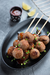 Black plate with nem nuong or fried vietnamese pork meatballs on skewers, closeup, vertical shot