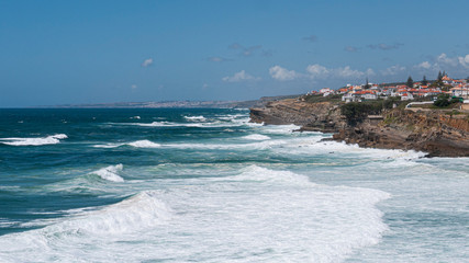 View of cliff top villas and the Atlantic ocean waves on a sunny summer day, taken in Praia das Ma&ccedil;&atilde;s, Sintra, Portugal