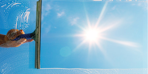 Fensterputzer putzt Fenster mit Schaum und Abzieher im Sonnenlicht - Panorama