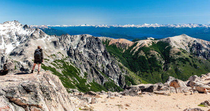 A young woman with backpack hiking and sitting on rocks and snow and enjoying the views of the Andes mountains and lake hiking Villa Catedral to Colonia Suiza in Patagonia, Argentina. Winter backpack