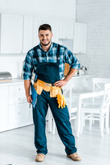 happy bearded workman standing with hand on hip and holding clipboard