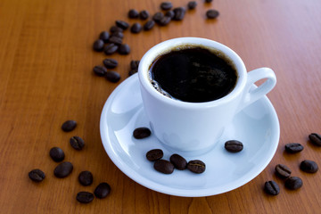 Black coffee in the white cup on the light brown wooden background. Copy space. Closeup.