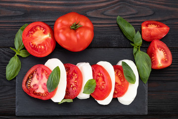 Caprese salad. Mozzarella cheese, tomatoes and basil herb leaves over stone table. Top view