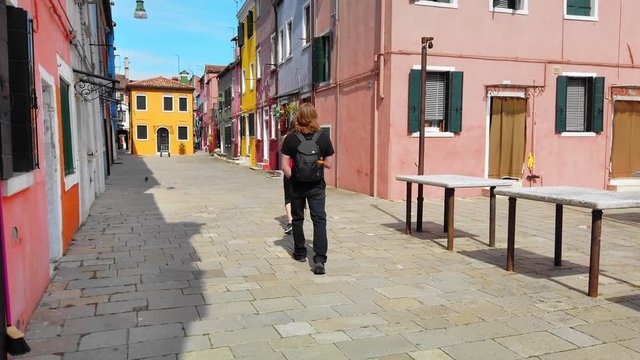 Burano, VENICE, Italy - May 2019: Two unrecognized tourists walk around the medieval city. Colorful houses. Slow motion.