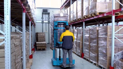 warehouse worker driver in uniform loading cardboard boxes by forklift stacker loader