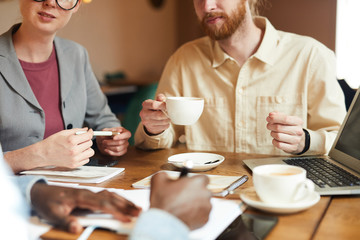 Close-up of business people sitting at the table and drinking coffee while their colleague signing a business document they have a business meeting