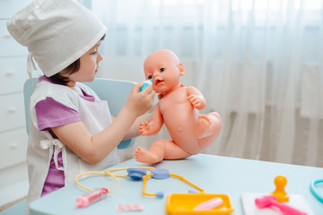 Little girl 3 years old preschooler playing doctor with doll. The child makes an injection toy.