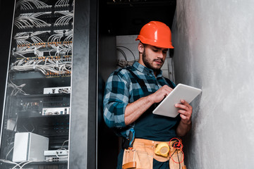 handsome bearded technician in safety helmet holding digital tablet