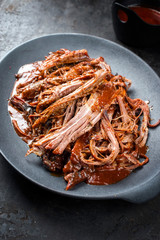 Traditional barbecue wagyu torn to bits pulled beef in hot chili sauce in a modern design cast iron plate as closeup on a rustic board with copy space