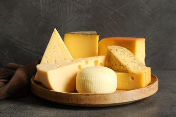 Wooden plate with different sorts of cheese on grey table