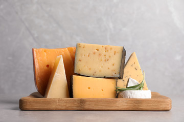 Wooden tray with different sorts of cheese and rosemary on grey table