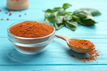 Glass bowl of red powdered pepper and spoon on blue wooden table, space for text