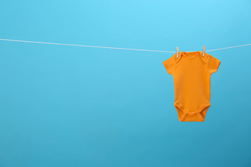 Baby onesie hanging on clothes line against blue background, space for text. Laundry day