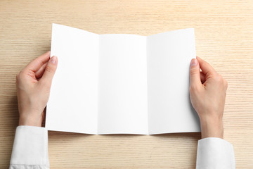 Obraz premium Young woman holding blank brochure at light wooden table, top view. Mock up for design