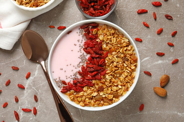 Smoothie bowl with goji berries and spoon on beige marble table, flat lay