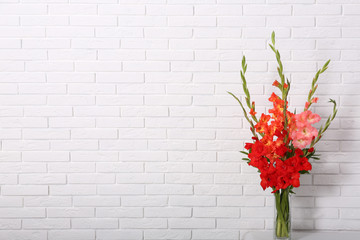 Vase with beautiful gladiolus flowers on table against white brick wall. Space for text - obrazy, fototapety, plakaty