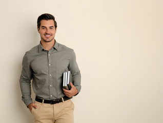 Young male teacher with books on beige background. Space for text