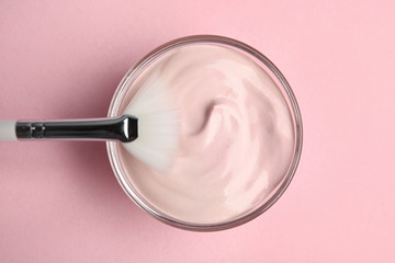 Professional face mask with brush on pink background, top view