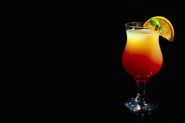 Glass of delicious cocktail Sex on the Beach decorated with orange and mint against black background. Space for text