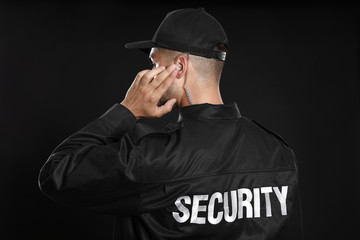 Male security guard in uniform using radio earpiece on dark background