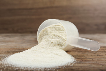 Overturned measuring scoop with protein powder on wooden table, closeup