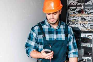 handsome technician holding digital meter near wires and cables