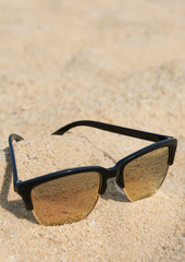 Sonnenbrille liegt im Sand, Hochformat
