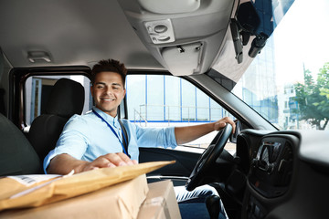 Young courier with parcels in delivery car