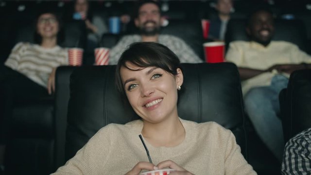 Slow motion portrait of cheerful young woman laughing watching film in cinema holding drink having fun with friends. People, youth and entertainment concept.