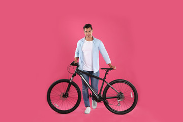 Handsome young man with modern bicycle on pink background